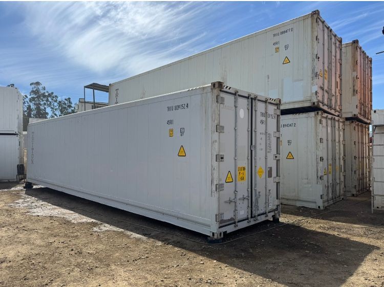 Stacked white shipping containers in an outdoor storage area under a blue sky.